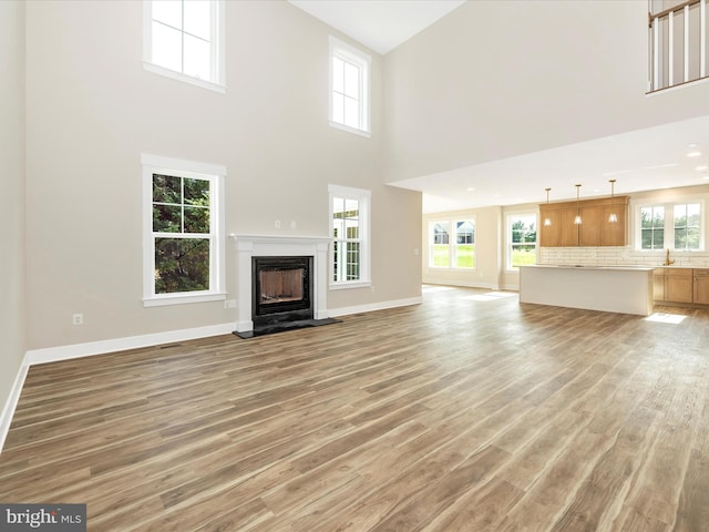 unfurnished living room with a fireplace, a high ceiling, baseboards, and light wood-style floors