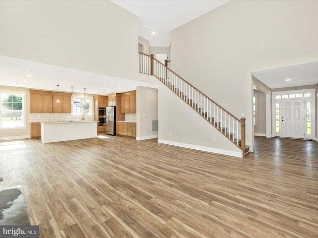 unfurnished living room featuring light wood finished floors, recessed lighting, stairs, baseboards, and a towering ceiling