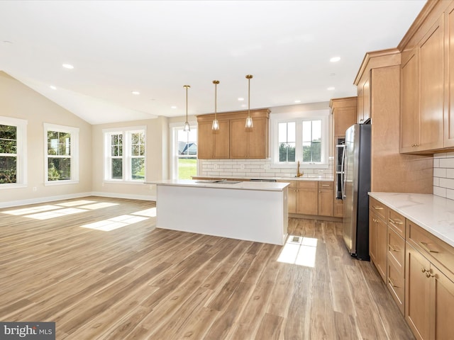 kitchen featuring light wood-style flooring, freestanding refrigerator, backsplash, a center island, and lofted ceiling