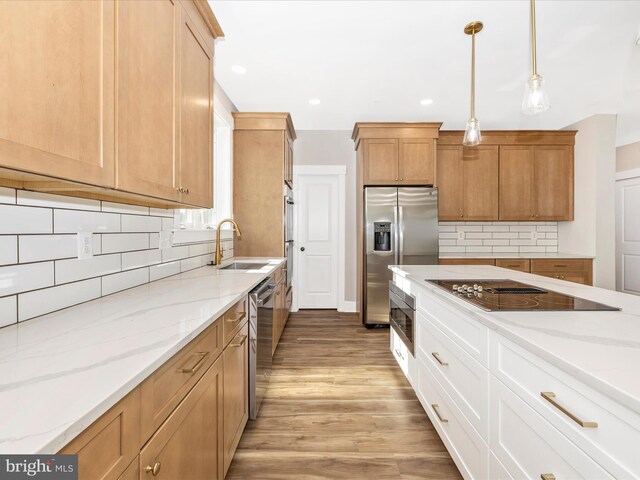 kitchen featuring a sink, appliances with stainless steel finishes, light wood-type flooring, light stone countertops, and backsplash