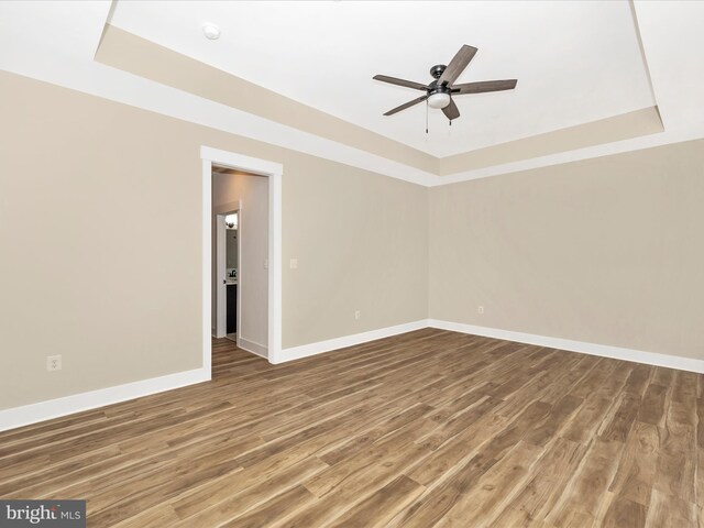 empty room featuring wood finished floors, a raised ceiling, ceiling fan, and baseboards