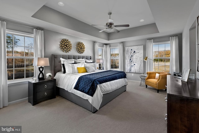carpeted bedroom with a tray ceiling, a ceiling fan, and baseboards