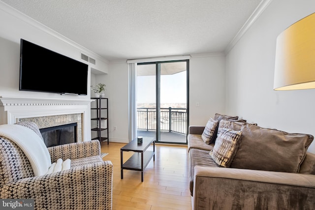 living room with crown molding, a textured ceiling, light wood-style floors, visible vents, and a high end fireplace