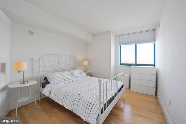 bedroom with light wood-style flooring, baseboards, and a textured ceiling