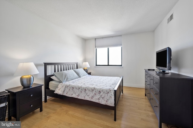 bedroom featuring baseboards, light wood-style floors, a textured ceiling, and visible vents