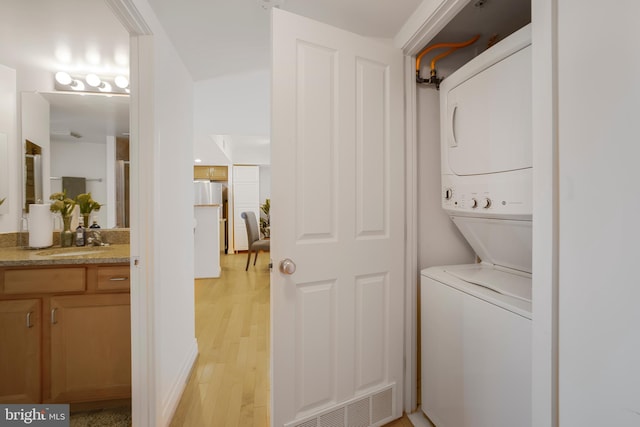 laundry room with visible vents, stacked washer / dryer, laundry area, a sink, and light wood-type flooring