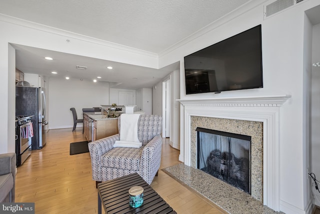 living area with a textured ceiling, a high end fireplace, visible vents, light wood-style floors, and ornamental molding