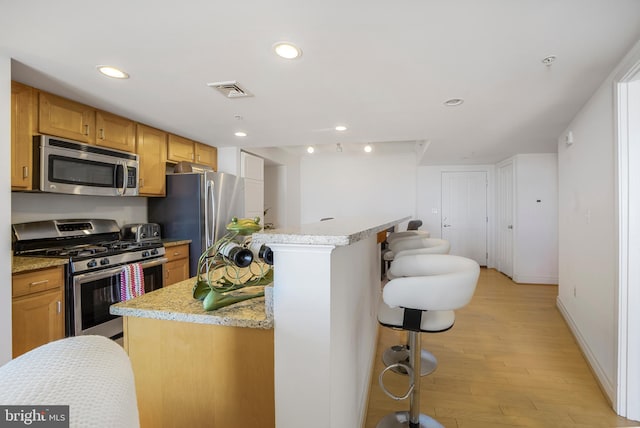 kitchen with a kitchen breakfast bar, appliances with stainless steel finishes, light wood-style flooring, visible vents, and recessed lighting