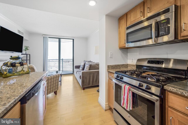kitchen featuring stainless steel appliances, stone counters, light wood-style floors, open floor plan, and brown cabinetry