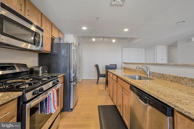 kitchen featuring light wood-type flooring, stainless steel appliances, a sink, light stone countertops, and brown cabinetry