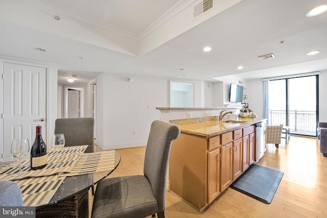 kitchen featuring light stone countertops, stainless steel dishwasher, light wood-style floors, visible vents, and a kitchen island with sink