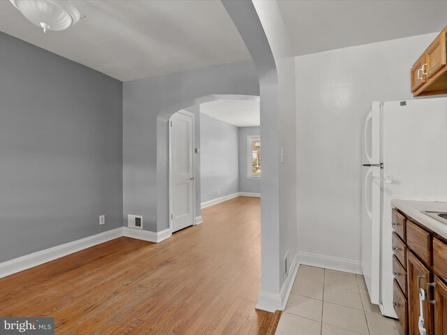 kitchen with arched walkways, freestanding refrigerator, baseboards, light wood-style floors, and light countertops