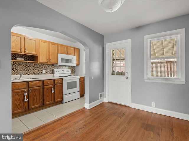 kitchen featuring white appliances, a sink, light countertops, light wood finished floors, and arched walkways