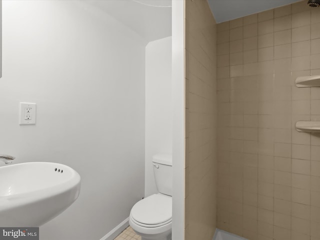 bathroom featuring a sink, toilet, baseboards, and tiled shower