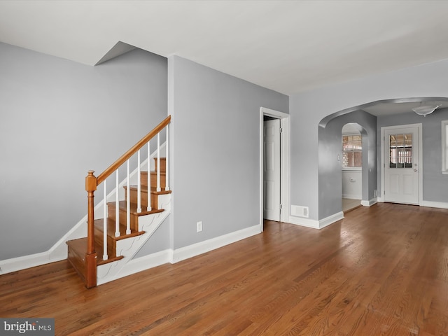 unfurnished living room with arched walkways, baseboards, wood finished floors, and stairway