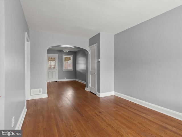 spare room featuring arched walkways, wood finished floors, and baseboards