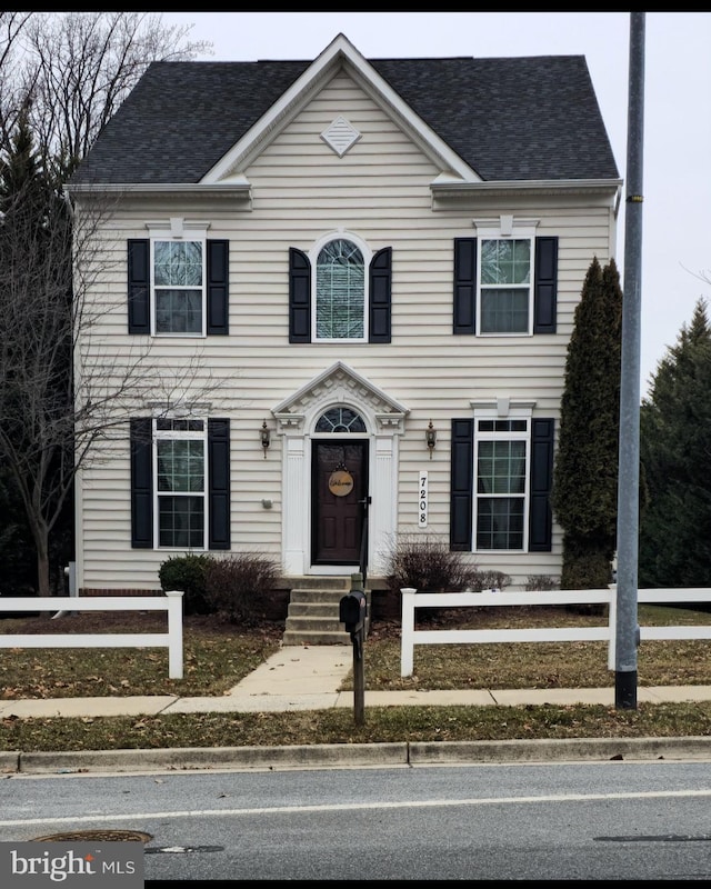 colonial home featuring a fenced front yard and roof with shingles