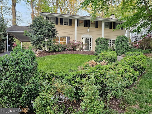 colonial-style house featuring a front lawn and a carport