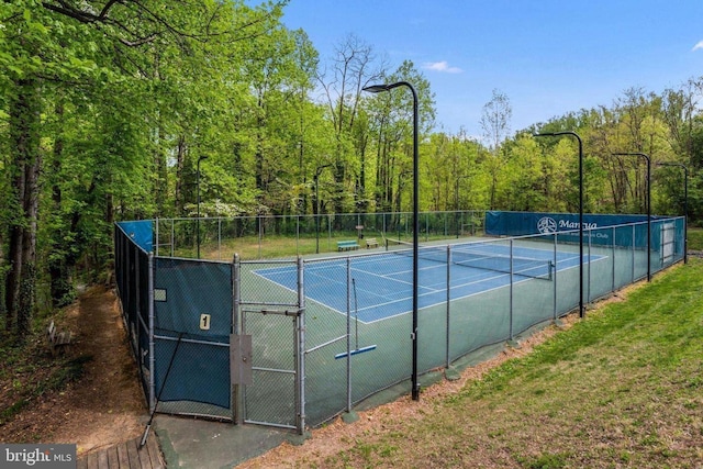 view of tennis court featuring a gate, fence, and a forest view