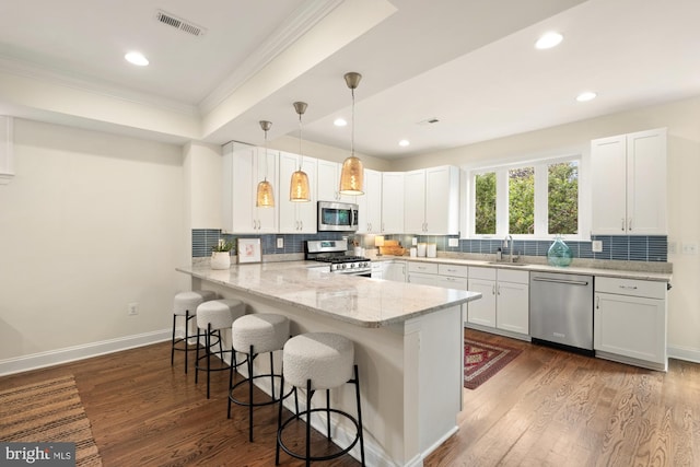 kitchen with stainless steel appliances, a sink, ornamental molding, a peninsula, and a kitchen bar