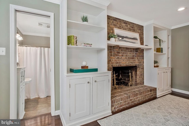living room featuring ornamental molding, baseboards, built in features, and a brick fireplace