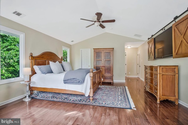 bedroom featuring multiple windows, lofted ceiling, wood finished floors, baseboards, and a barn door