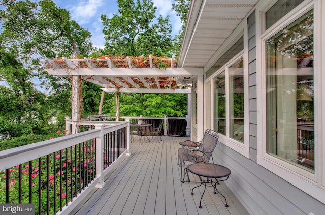 wooden deck with a pergola, outdoor dining area, and view of scattered trees