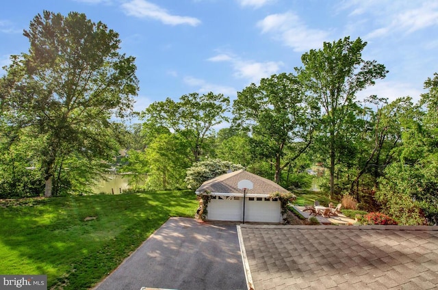view of front of property featuring driveway, an outdoor structure, a garage, a front lawn, and a shingled roof