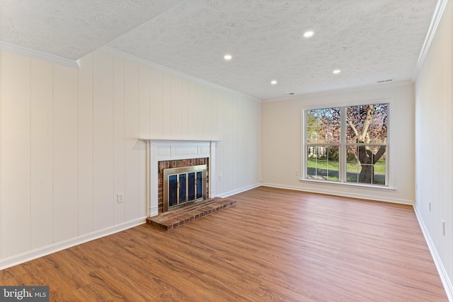 unfurnished living room with a textured ceiling, wood finished floors, a brick fireplace, and ornamental molding