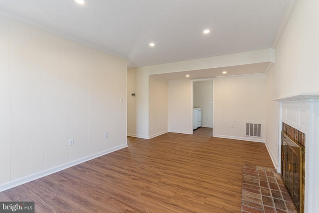 unfurnished living room with a tiled fireplace, baseboards, visible vents, wood finished floors, and ornamental molding
