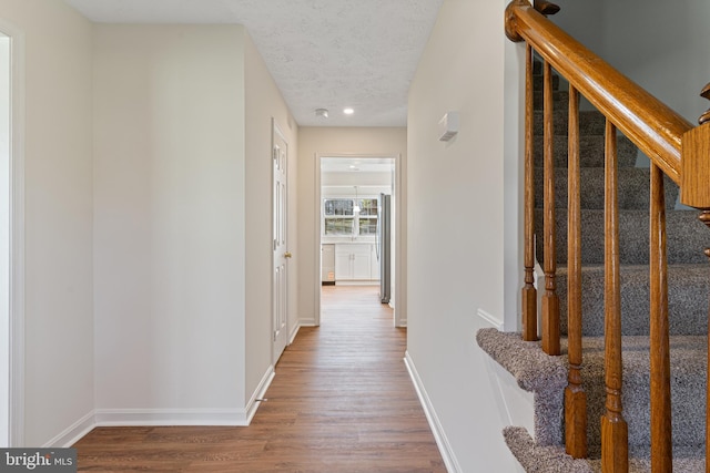 hall with baseboards, wood finished floors, a textured ceiling, and stairway