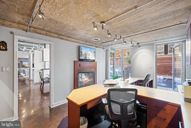 home office featuring track lighting, finished concrete flooring, baseboards, and a glass covered fireplace