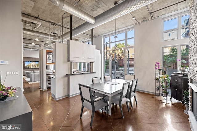 dining room featuring a towering ceiling, concrete flooring, baseboards, and a healthy amount of sunlight