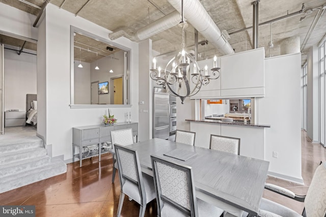dining room with baseboards, a notable chandelier, concrete floors, and a high ceiling