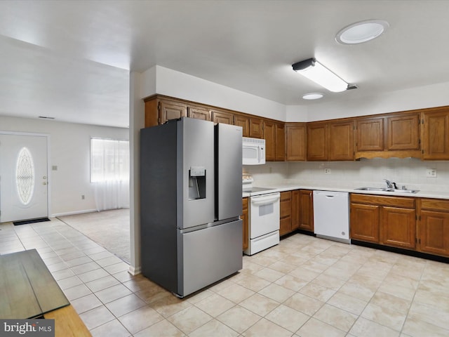 kitchen with a sink, light countertops, white appliances, brown cabinetry, and decorative backsplash