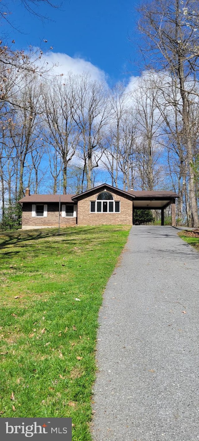 view of front facade with a front lawn, an attached carport, driveway, a chimney, and brick siding