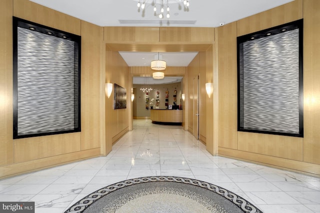 hall featuring marble finish floor, wood walls, and an inviting chandelier