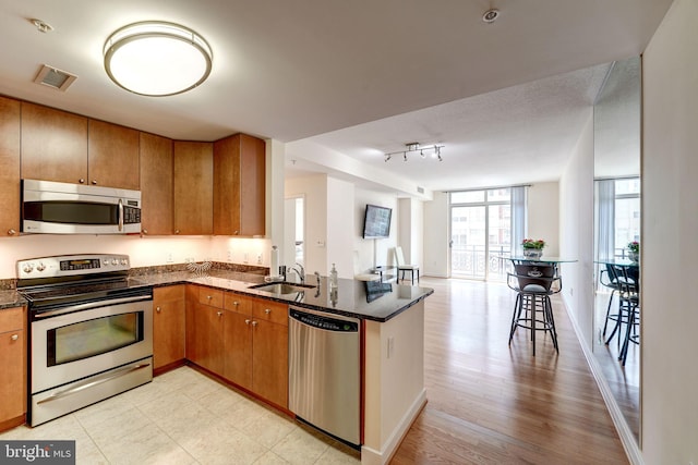 kitchen with a sink, open floor plan, stainless steel appliances, dark stone counters, and a peninsula