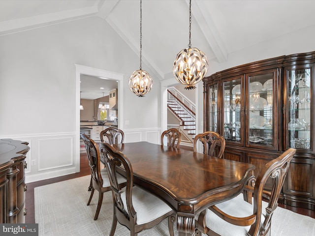 dining space featuring a wainscoted wall, vaulted ceiling with beams, an inviting chandelier, and wood finished floors