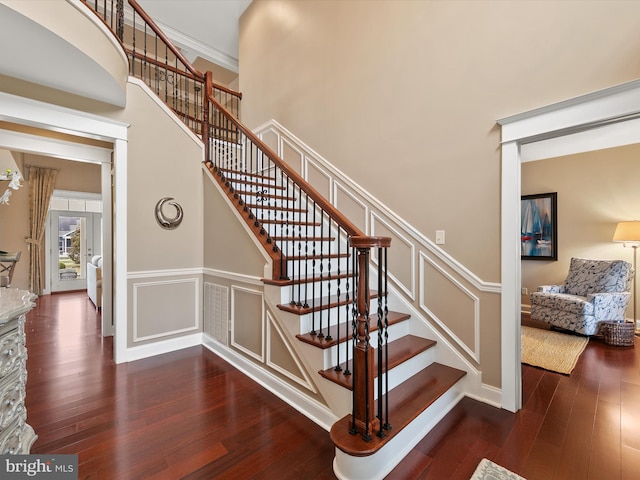 staircase featuring wood finished floors, a towering ceiling, and a decorative wall