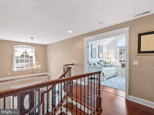 hallway with visible vents, an upstairs landing, wood finished floors, baseboards, and a chandelier