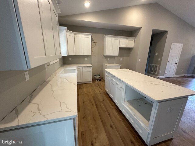 kitchen with light stone counters, white cabinetry, lofted ceiling, and wood finished floors
