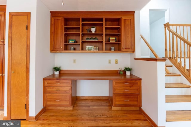 interior space featuring built in desk, baseboards, and light wood-style floors