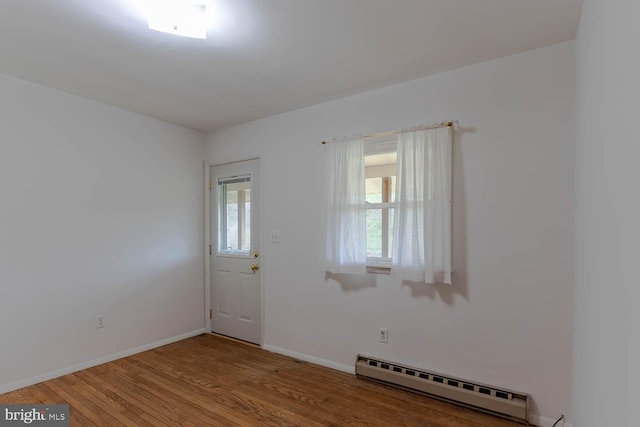 unfurnished room with wood finished floors, a baseboard heating unit, and baseboards
