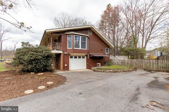 view of side of home with aphalt driveway, a garage, fence, and a balcony