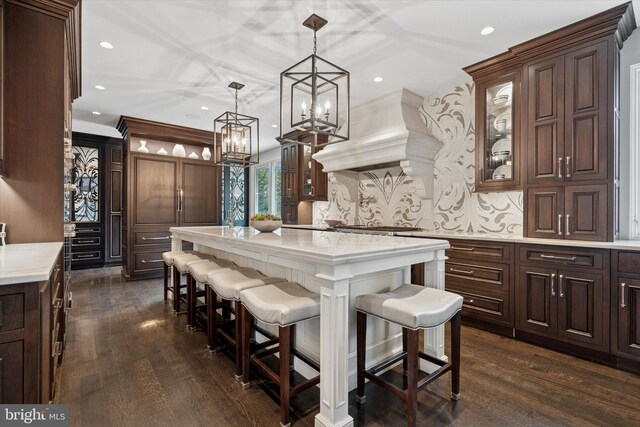 kitchen featuring a kitchen island, dark brown cabinets, glass insert cabinets, a kitchen bar, and custom range hood