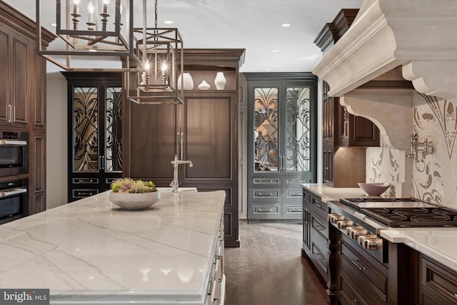 kitchen featuring dark brown cabinets, light stone countertops, multiple ovens, and stainless steel gas stovetop