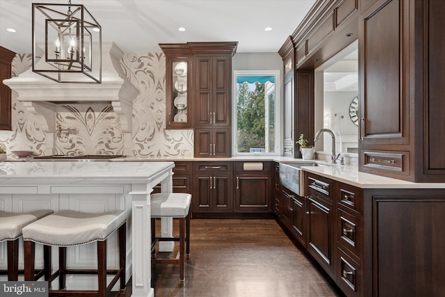 interior space with dark wood-style flooring, dark brown cabinets, a sink, light countertops, and a kitchen breakfast bar