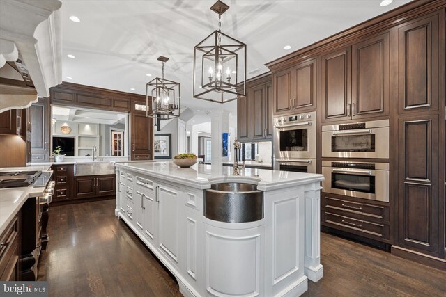 kitchen featuring dark wood-type flooring, an island with sink, a notable chandelier, and stainless steel appliances