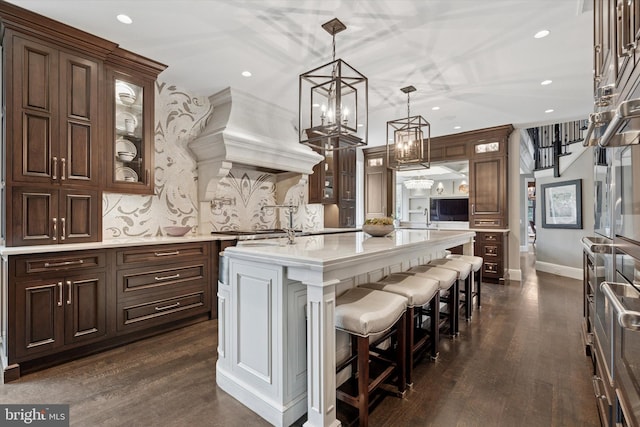 kitchen with a breakfast bar area, a center island with sink, recessed lighting, pendant lighting, and glass insert cabinets